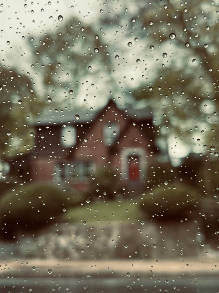 pexels-photo-16651271-16651271 Artistic photo capturing raindrops on a window with a blurred house in the background.